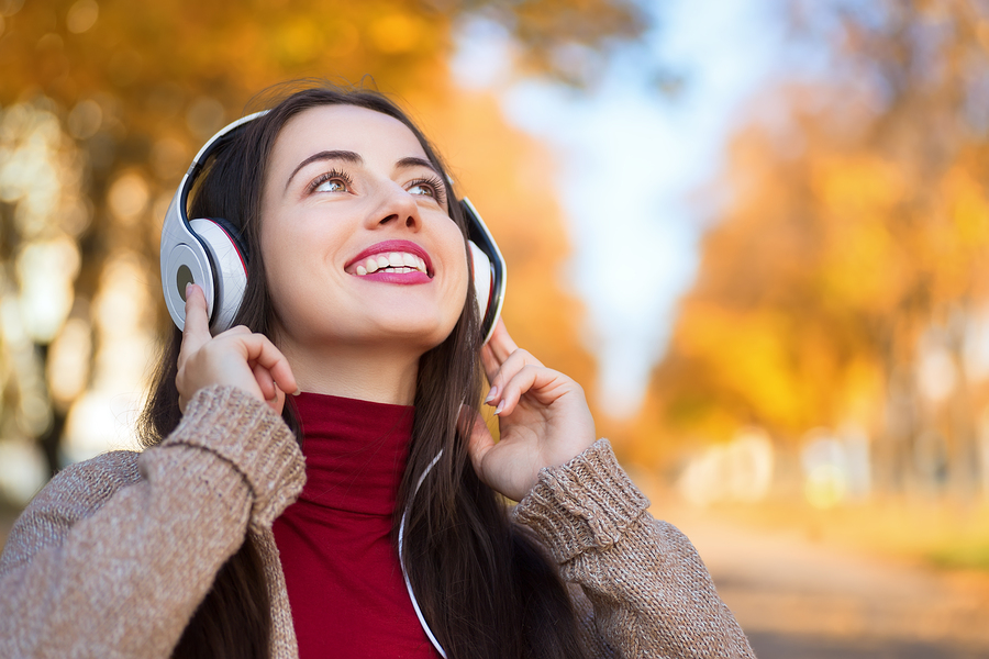 Young happy smiling brunette woman with headphones outdoors on autumn day.