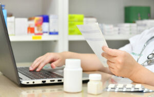 Image shows pharmacist at computer labeling prescriptions.