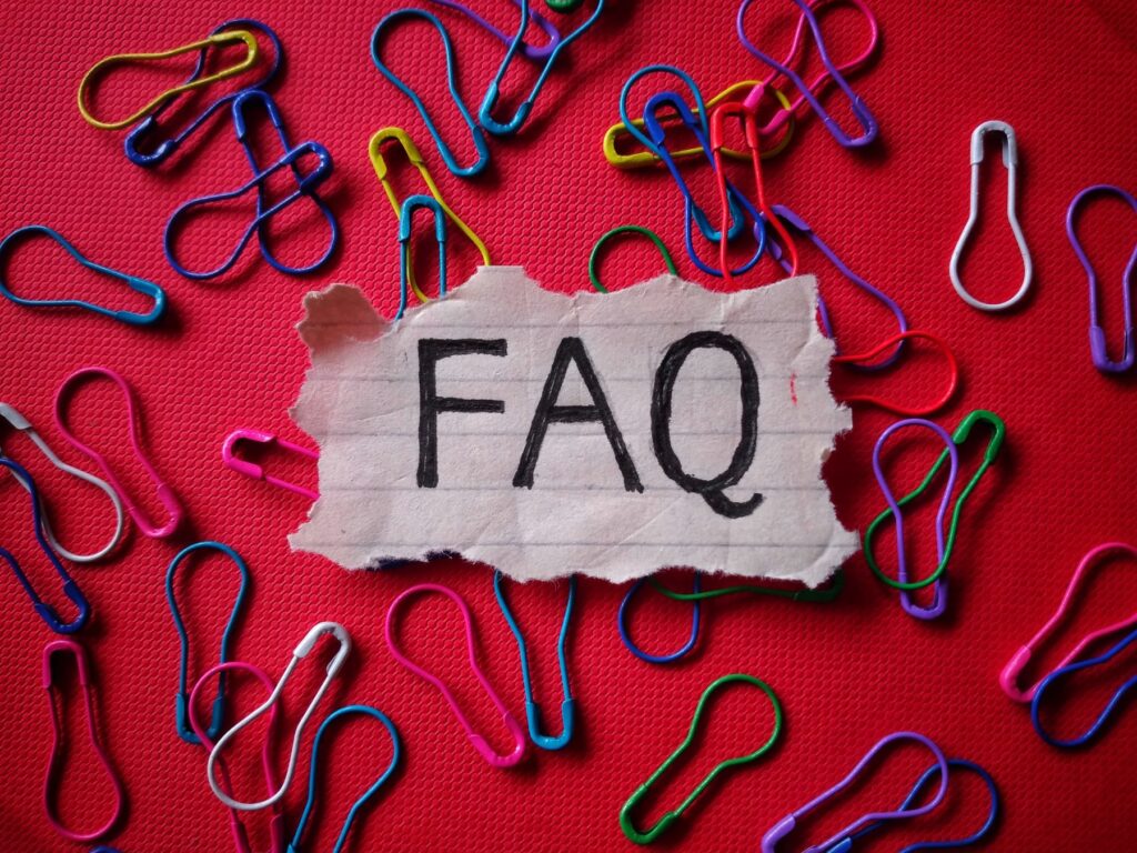 FAQ written on note sitting on red background with bright paper clips