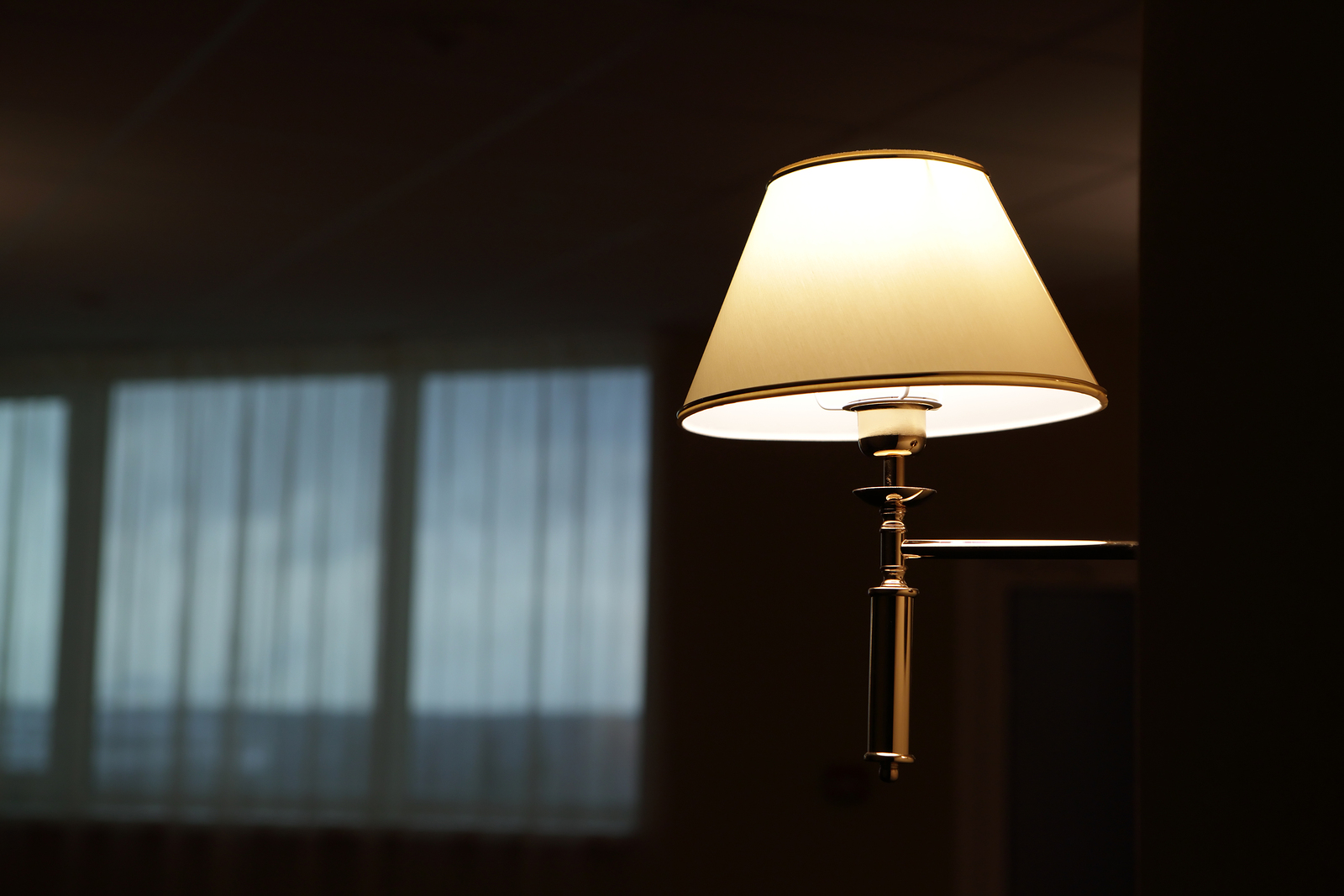 A stand lamp with the light on in a dark living room.