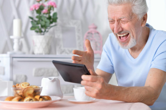 Image shows older man happily using a tablet.