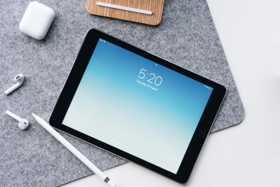 Image shows: Apple iPad and AirPods on a gray mat