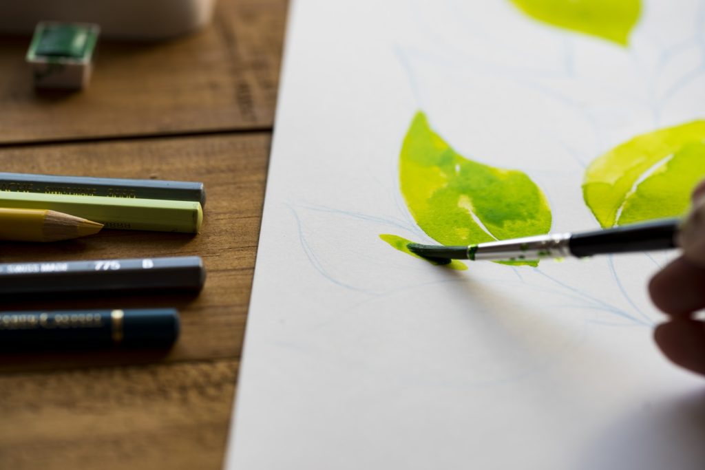 Closeup of green leaves being painted, with pencils next to the painting.