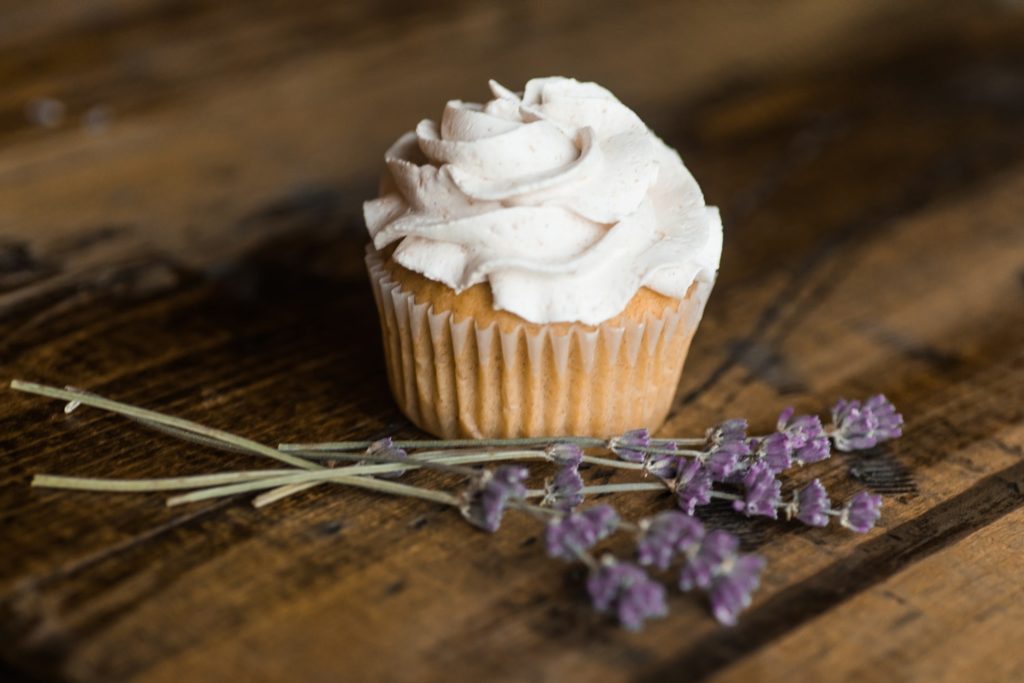 Cupcake with icing, next to sprigs of dried lavender, on a wooden table.