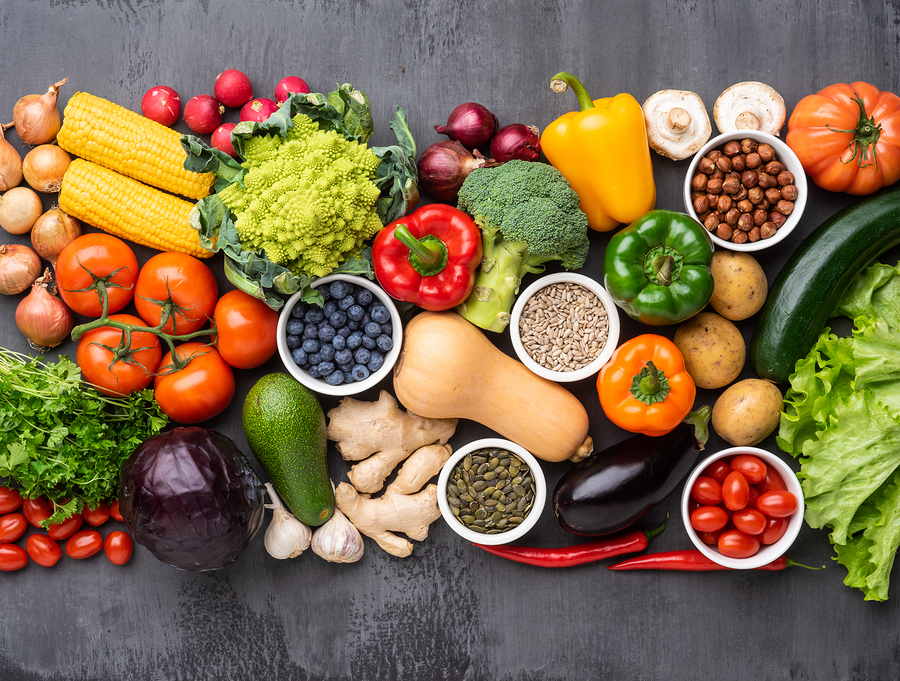 Fresh vegetables and fruits spread out on a gray table.