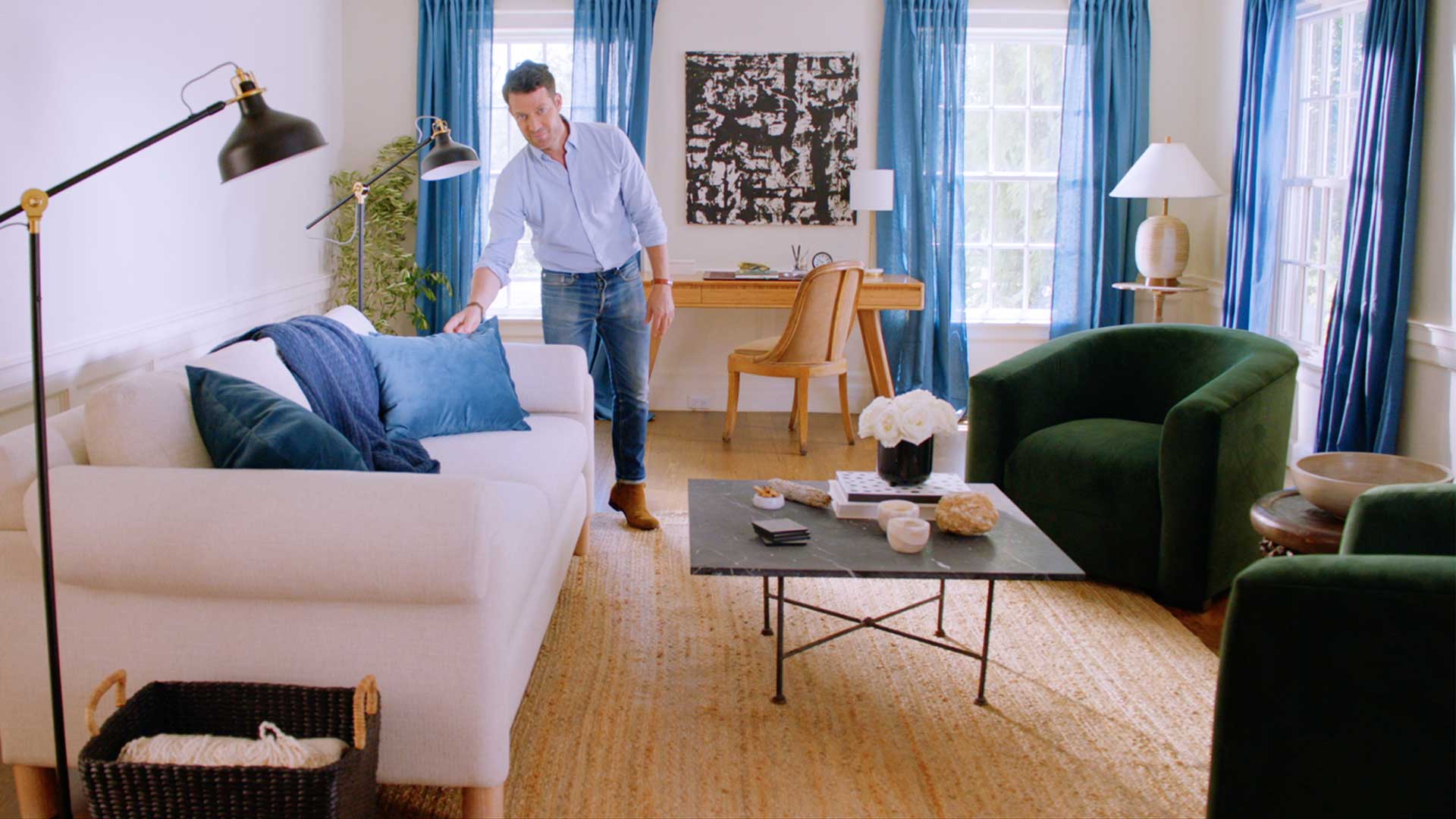 Nate Berkus fixing up a blue pillow on a couch in a living room.