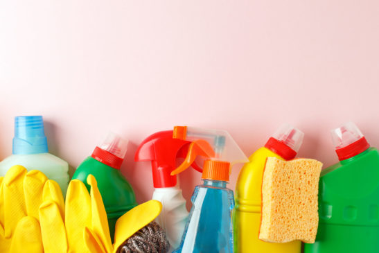 Colorful cleaning supplies on a light pink background.