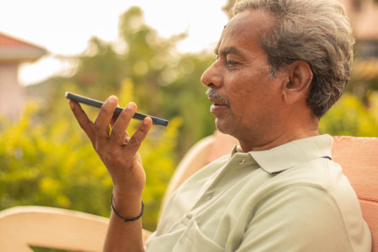 Senior man talking using smartphone voice assistant outdoors.