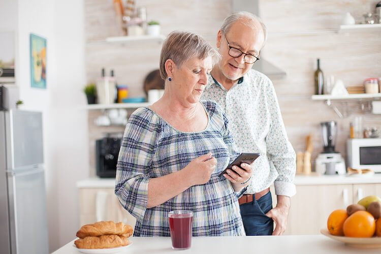 Image shows: Woman teaching man to use app on smartphone.