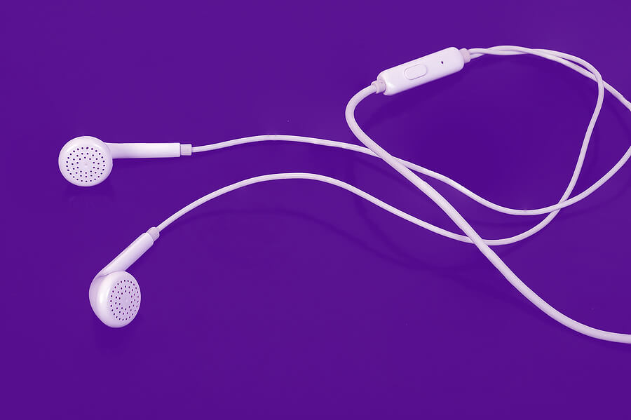 Image shows white wired ear buds on bright purple background.