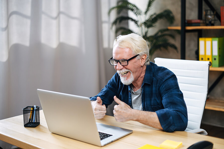 Senior man at computer smiling and giving two handed thumbs up sign of success.