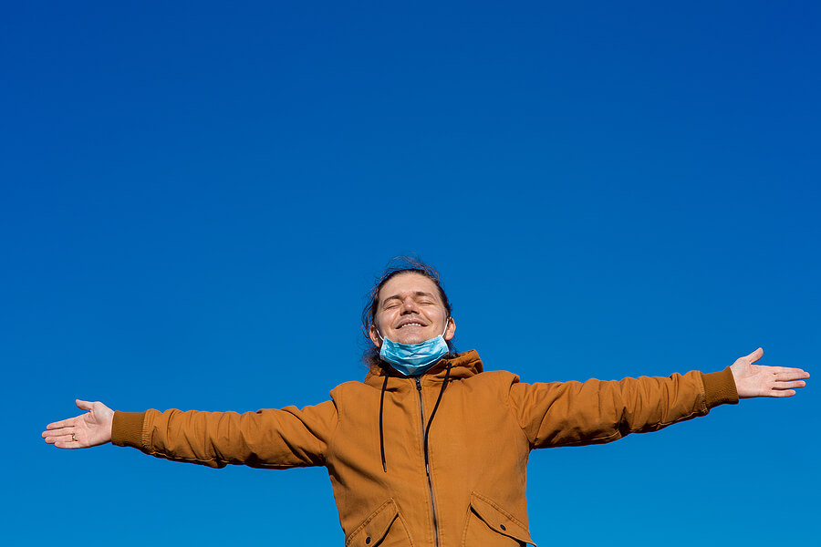 Image shows smiling man, arms outstretched, mask off face.