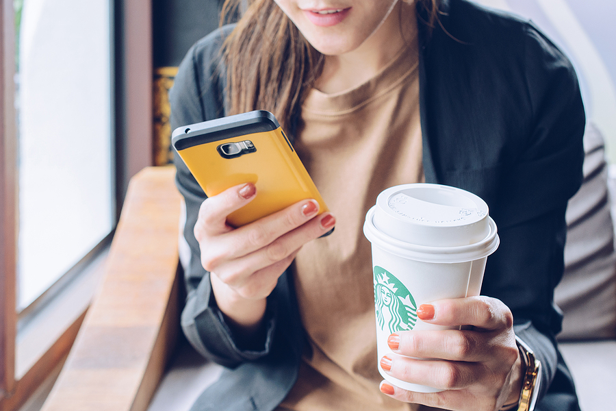 Image shows woman holding mobile phone and cuts of coffee from Starbucks.
