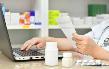 Image shows pharmacist at computer labeling prescriptions.