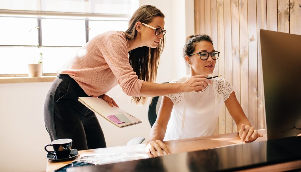 Two female coworkers working and looking at computer monitor.