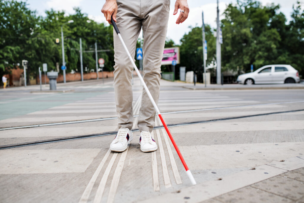 Visually impaired person with white cane crossing city street