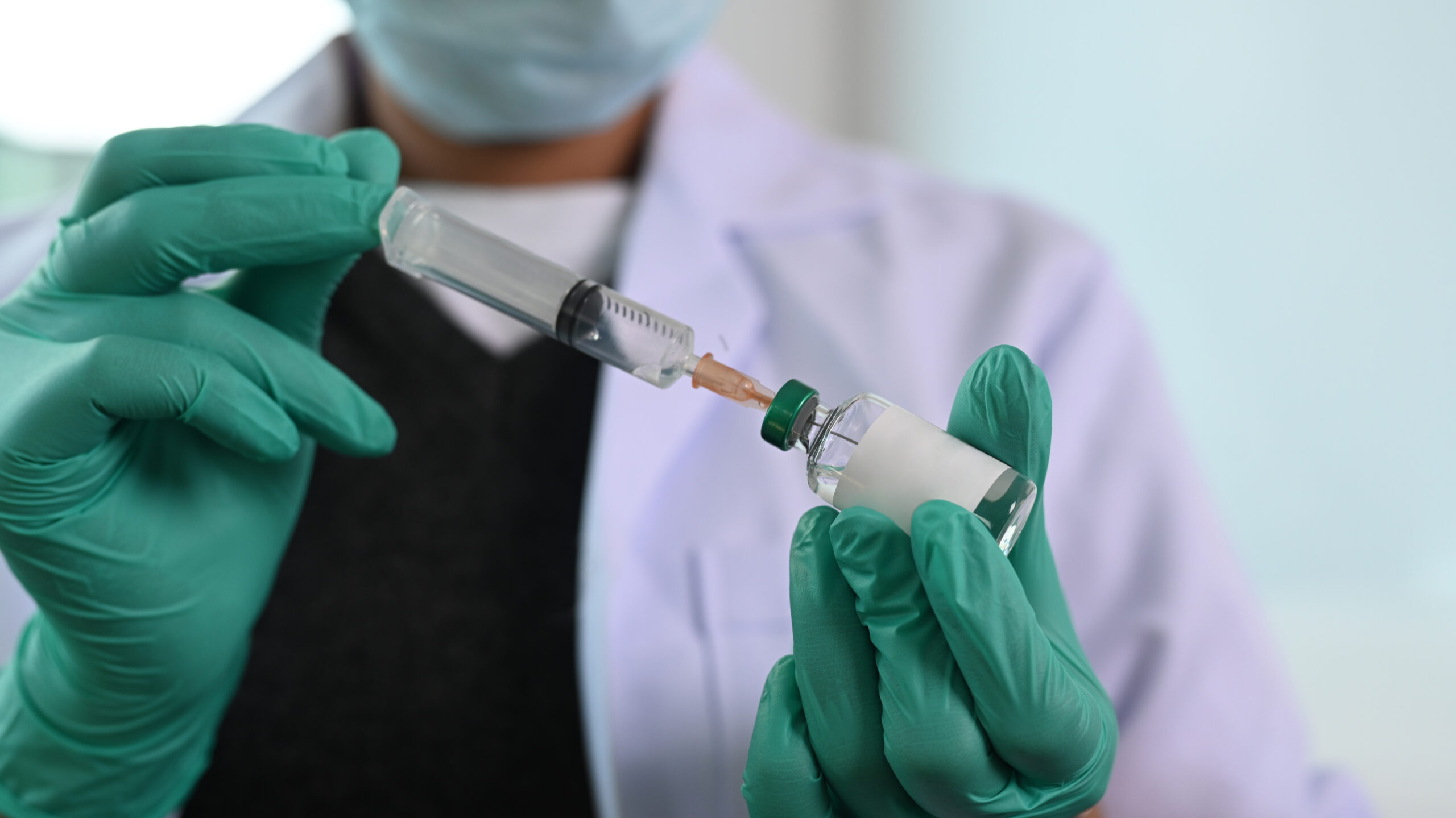 Closeup of doctor’s gloved hands holding needle syringe