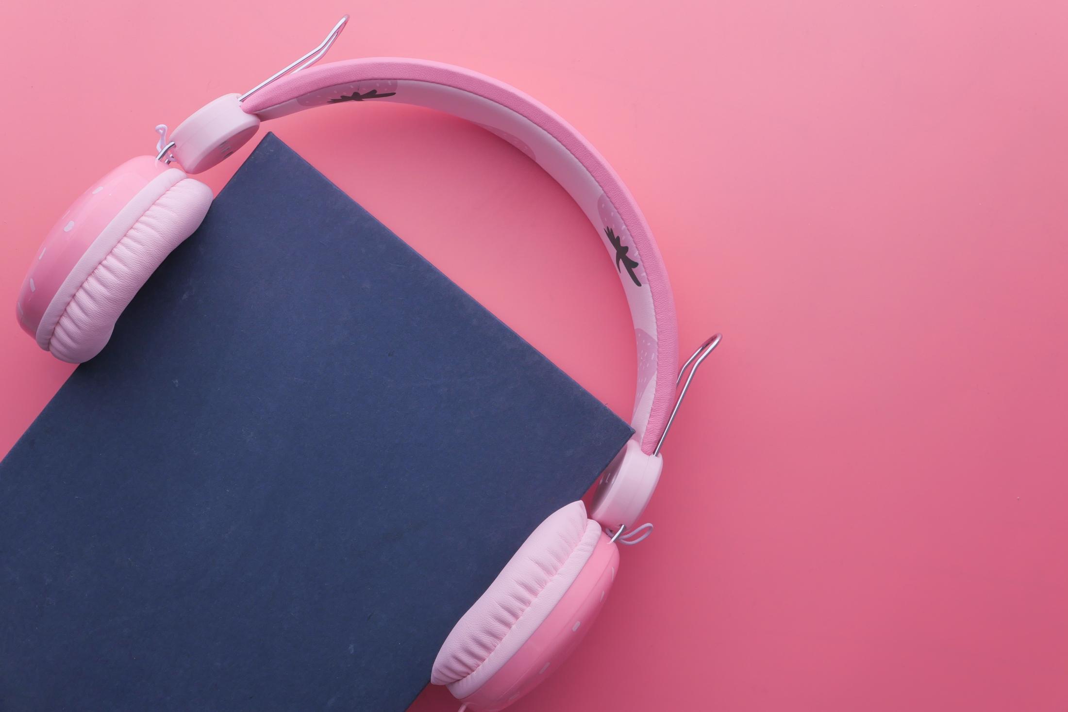 Magazine binder with white headphones on pink background