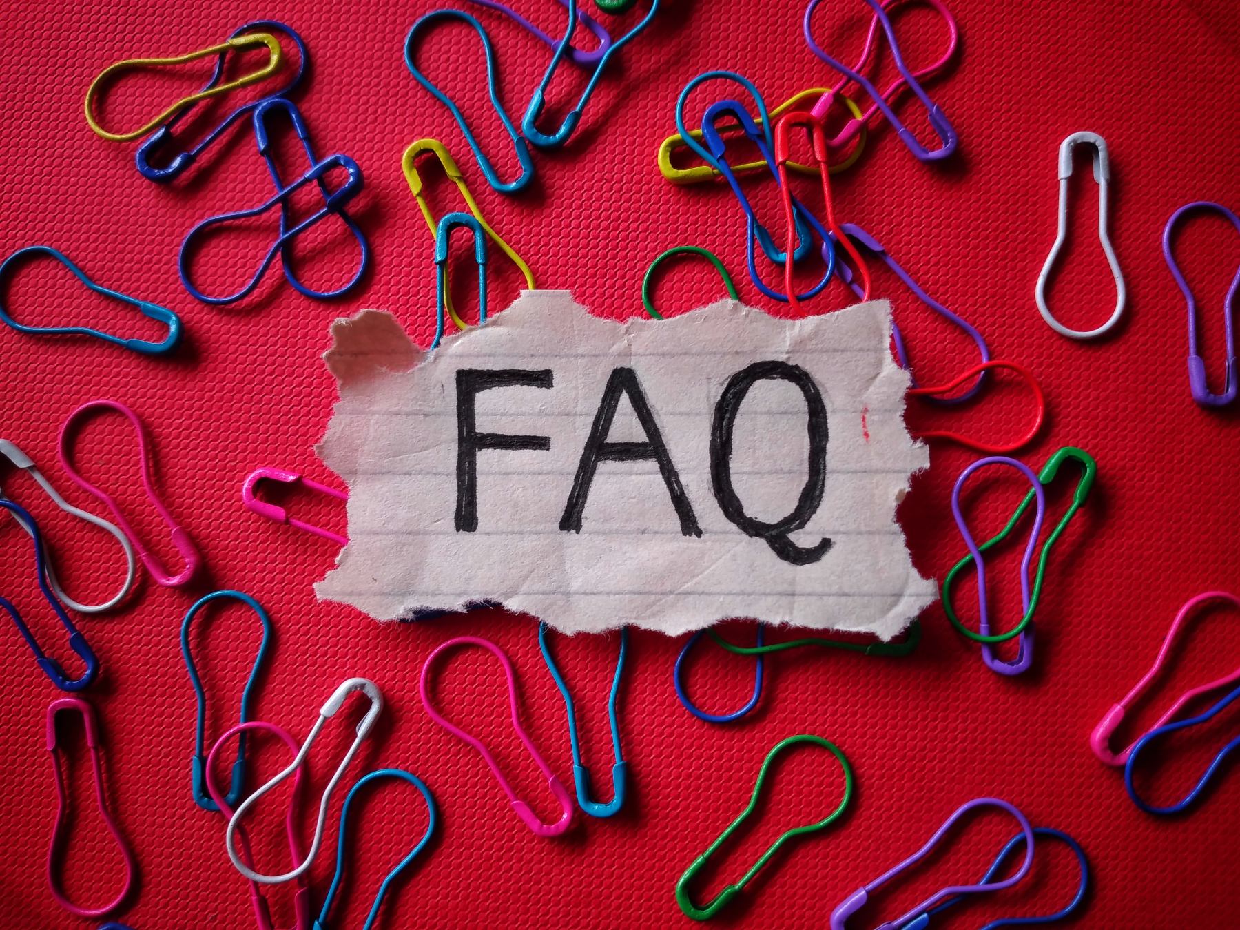 FAQ written on note sitting on red background with bright paper clips